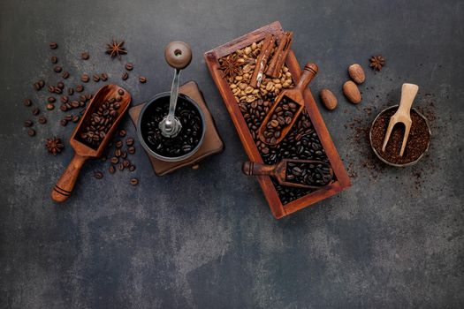 Various of roasted coffee beans in wooden box with manual coffee grinder setup on dark stone background.