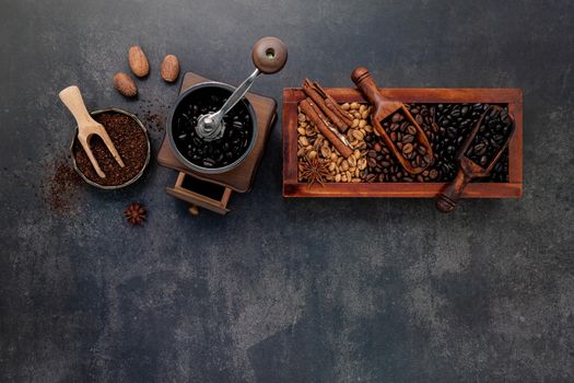 Various of roasted coffee beans in wooden box with manual coffee grinder setup on dark stone background.