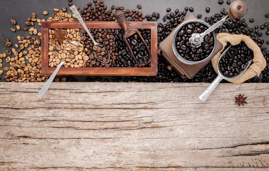 Various of roasted coffee beans in wooden box with manual coffee grinder setup on shabby wooden background.