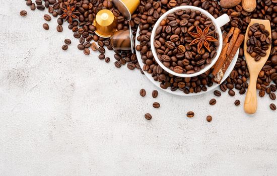 Background of dark roasted coffee beans and capsules with scoops setup on white concrete background with copy space.