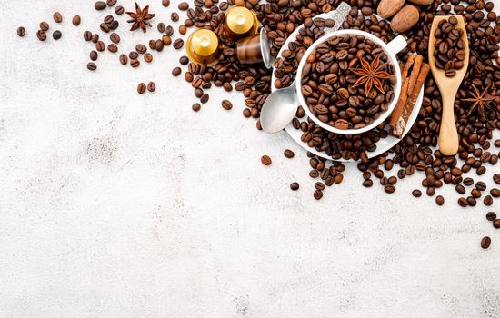 Background of dark roasted coffee beans and capsules with scoops setup on white concrete background with copy space.