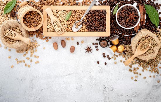 Green and brown decaf unroasted and dark roasted coffee beans in wooden box with scoops setup on white concrete background.