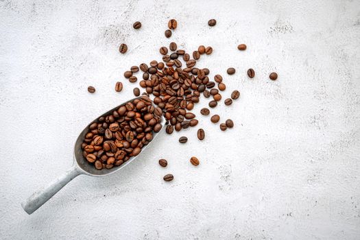 Roasted coffee beans with scoops setup on white concrete background.