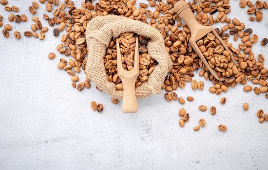 Roasted coffee beans with scoops setup on white concrete background.