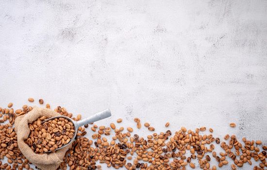 Roasted coffee beans with scoops setup on white concrete background.