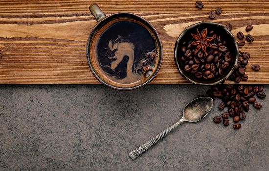 Roasted coffee beans with coffee cup setup on dark stone background.