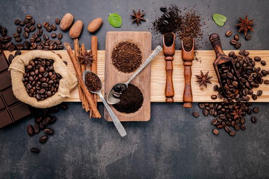 Roasted coffee beans with coffee powder and flavourful ingredients for make tasty coffee setup on dark stone background.