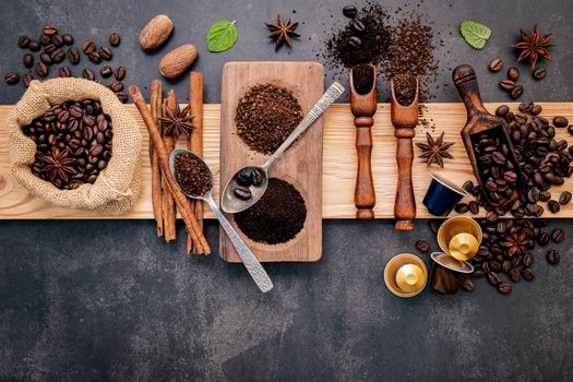 Roasted coffee beans with coffee powder and flavourful ingredients for make tasty coffee setup on dark stone background.