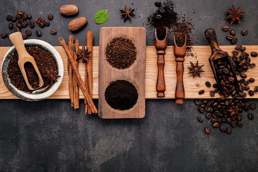 Roasted coffee beans with coffee powder and flavourful ingredients for make tasty coffee setup on dark stone background.