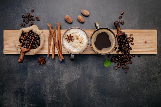 Roasted coffee beans with coffee powder and flavourful ingredients for make tasty coffee setup on dark stone background.