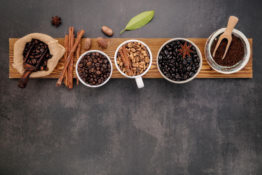 Brown unroasted and dark roasted coffee beans in coffee cup with scoops setup on dark stone background.