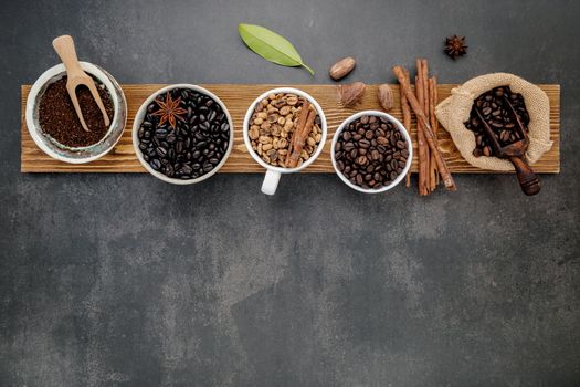 Brown unroasted and dark roasted coffee beans in coffee cup with scoops setup on dark stone background.