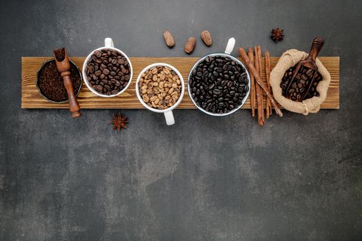 Brown unroasted and dark roasted coffee beans in coffee cup with scoops setup on dark stone background.