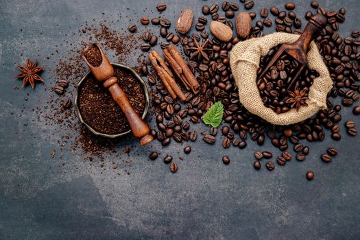 Roasted coffee beans with coffee powder and flavourful ingredients for make tasty coffee setup on dark stone background.