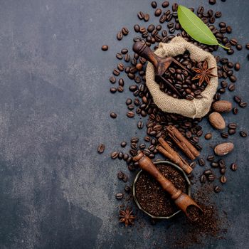 Roasted coffee beans with coffee powder and flavourful ingredients for make tasty coffee setup on dark stone background.