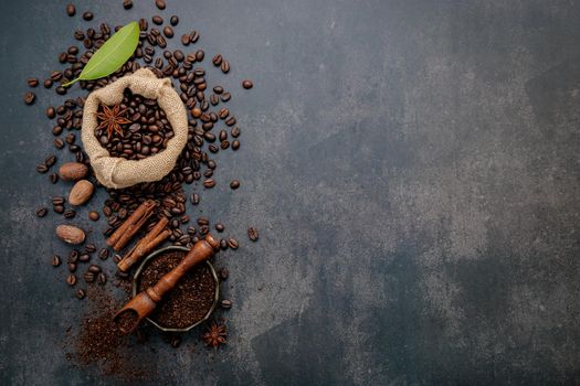 Roasted coffee beans with coffee powder and flavourful ingredients for make tasty coffee setup on dark stone background.