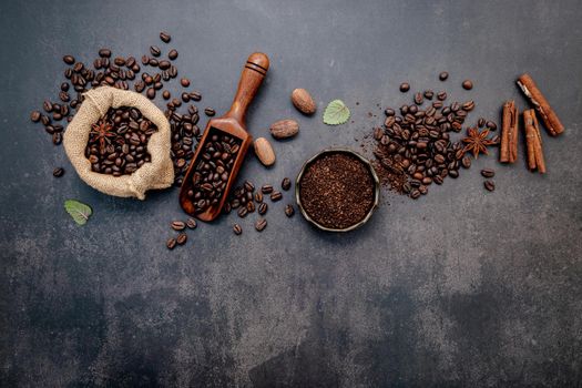 Roasted coffee beans with coffee powder and flavourful ingredients for make tasty coffee setup on dark stone background.