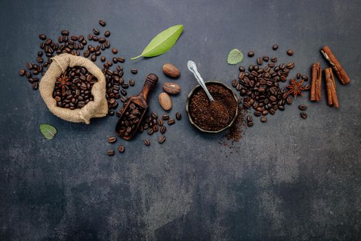 Roasted coffee beans with coffee powder and flavourful ingredients for make tasty coffee setup on dark stone background.