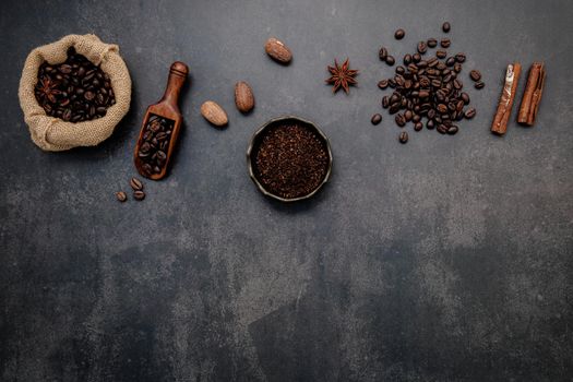 Roasted coffee beans with coffee powder and flavourful ingredients for make tasty coffee setup on dark stone background.