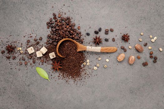 Green and brown unroasted and dark roasted coffee beans in wooden bowl with spoons set up on dark concrete background.