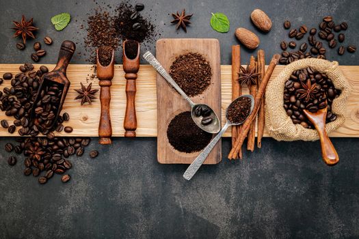 Roasted coffee beans with coffee powder and flavourful ingredients for make tasty coffee setup on dark stone background.