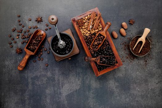 Various of roasted coffee beans in wooden box with manual coffee grinder setup on dark stone background.