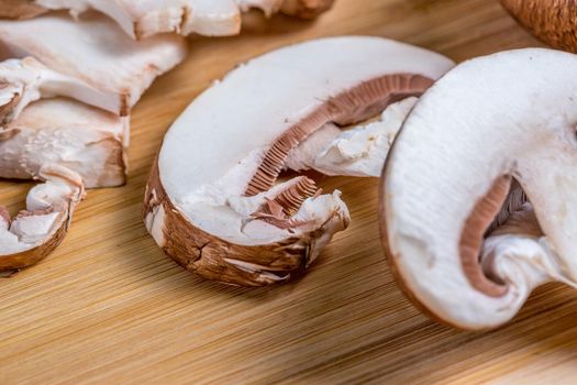 Royal champignons, Parisian champignons, chopped mushrooms on bamboo wooden chopping board, close-up. Dark wooden background. Side view.