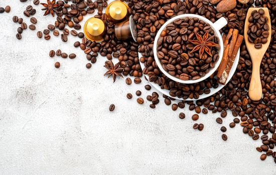 Background of dark roasted coffee beans and capsules with scoops setup on white concrete background with copy space.