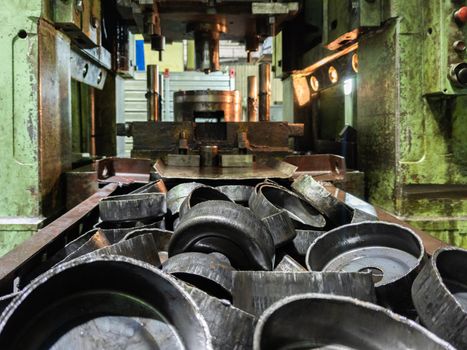 pile of stamped thick sheet black metal round parts after a hood operation in front of old blurred forming press with die tooling