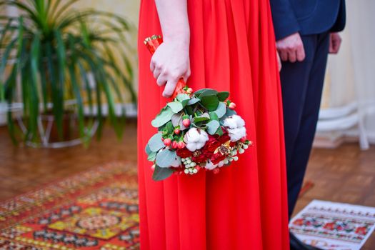 The wedding ceremony of the bride and groom. A bouquet of flowers in the hands of the bride. The bride in the red dress. Without faces.