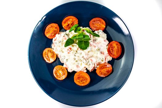 Russian salad on blue plate with cherry tomatoes on white background