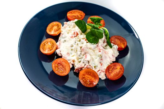 Russian salad on blue plate with cherry tomatoes on white background