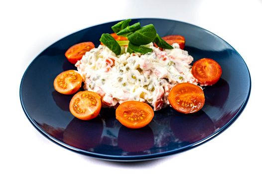 Russian salad on blue plate with cherry tomatoes on white background