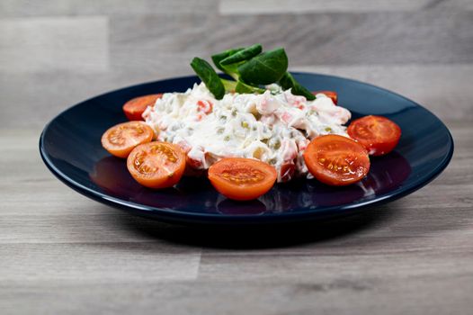 Russian salad in blue plate with cherry tomatoes on wooden background