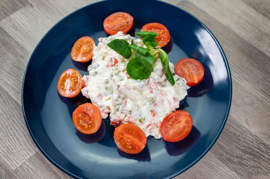 Russian salad in blue plate with cherry tomatoes on wooden background