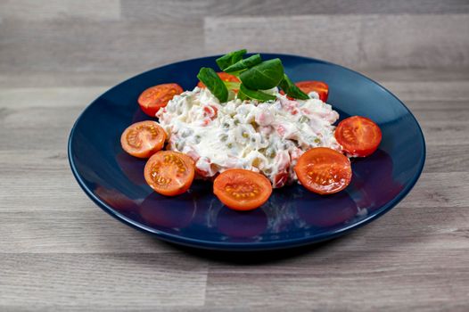 Russian salad in blue plate with cherry tomatoes on wooden background