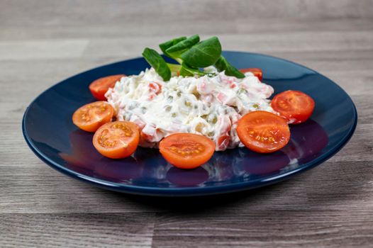 Russian salad in blue plate with cherry tomatoes on wooden background