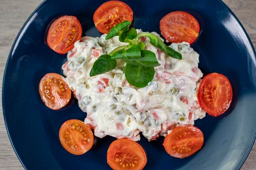 Russian salad in blue plate with cherry tomatoes on wooden background