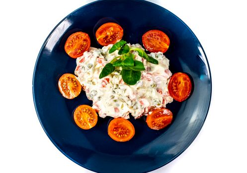 Russian salad on blue plate with cherry tomatoes on white background