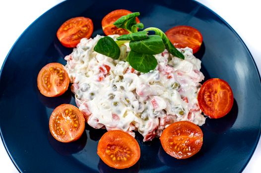 Russian salad on blue plate with cherry tomatoes on white background