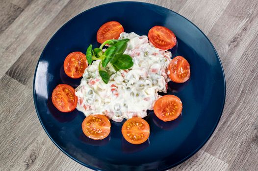Russian salad in blue plate with cherry tomatoes on wooden background