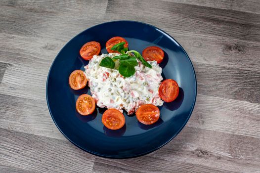 Russian salad in blue plate with cherry tomatoes on wooden background