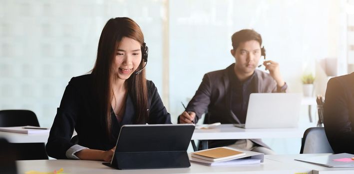 Young asian woman working in call centre, surrounded by colleagues