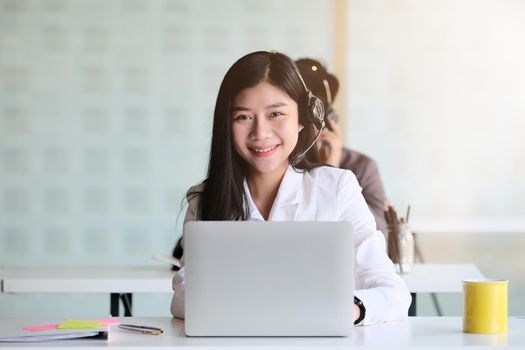 Portrait of young asian woman working in call centre, surrounded by colleagues