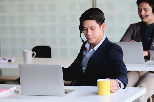 Asian businessman in headphones looking at laptop, watching good webinar, consulting client, distance learning languages, making notes, happy man participating online conference