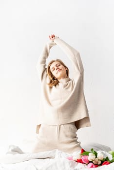 Smiling young woman wearing pajamas stretching on the bed in the morning