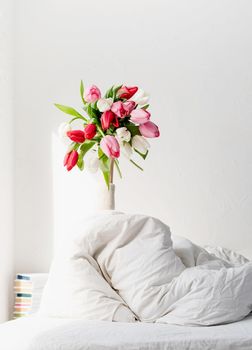 Woman arm outstreched from the blanket holding a bouquet of tulip flowers. Woman in bed holding tulip flowers