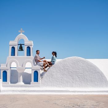 Santorini Greece, young couple mid age European and Asian on vacation at the Greek village of Oia Santorini Greece, luxury vacation Santorini. mid age man and woman watching sunset Santorini