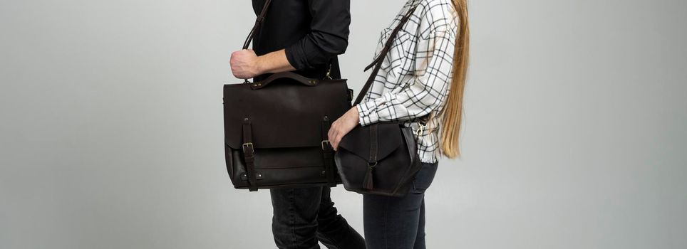 Brown men's shoulder leather bag for a documents and laptop holds by man in a black shirt and woman with a black small bag. Style, retro, fashion, vintage and elegance