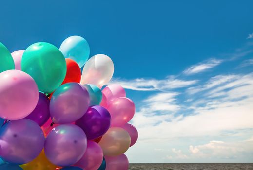 Lots of colorful balloons on the blue sky background with clouds and sea